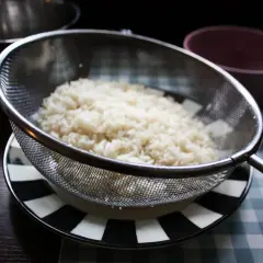 Ris i durkslag, redo att sköljas. För att koka ris med mycket vatten är det viktigt att skölja det först.