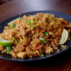 En tallrik med stekt ris med tofu, grönsaker och limeklyftor.