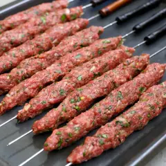 Råa kebabspett med lök och persilja ligger redo på en plåt för att tillagas i ugn.