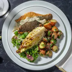 En tallrik med havsabborre, rostade potatisar, sallad och en bit grillad kål. Ett perfekt havsabborre recept för en fin middag.