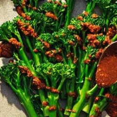 Ånga broccoli med en kryddig sås. En sked häller över mer sås på de gröna buketterna.
