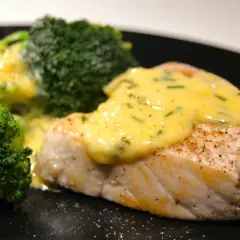 En saftig fiskfilé med krämig sås till tonfisk och gröna broccolibuketter på en svart tallrik.