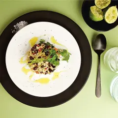 En portion gallo pinto med ris och svarta bönor, garnerad med koriander och en oljedressing. Serveras med limeklyftor och en drink med is.