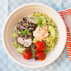 En skål med tillagad quinoa, skivat kött med sesamfrön, hummus, gurka och körsbärstomater. Perfekt för en snabb och hälsosam lunch.