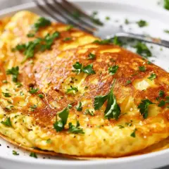En gyllene omelett, perfekt för ett snabbt omelett recept. Garnerad med färsk persilja och serverad på en vit tallrik med en gaffel.