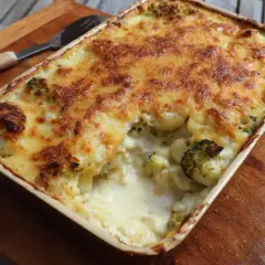 En ugnsform med ostgratinerad blomkål och broccoli, gyllene och bubblande. En sked ligger bredvid.