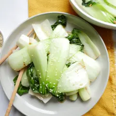 Enkel pak choi recept med sesamfrön. Grönsakerna är serverade på en tallrik med ätpinnar.