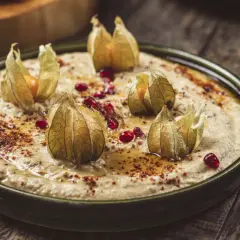 Krämig baba ganoush toppad med physalis och granatäppelkärnor, serverad på en rustik träyta.