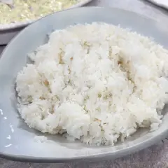 Perfekt fluffigt ris, enkelt att laga mat i riskokare. En skål med vitt ris står framför en annan skål med mat.