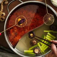 En person lägger ner grönsaker i en hot pot med två olika buljonger. Ett perfekt hot pot recept för en mysig kväll.