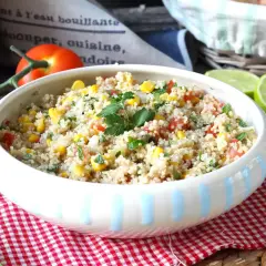 En skål med färgglad quinoa sallad med majs, tomat och persilja, garnerad med limeklyftor.
