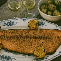 En stor grillad laxsida med citronklyftor på ett vackert fat. Serveras med dillpotatis, vit sås och vitt vin.
