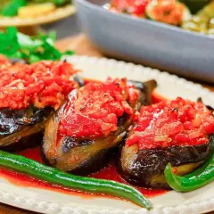 Tre auberginehalvor fyllda med tomat och paprika, serverade med gröna chilis. En härlig imam bayildi.