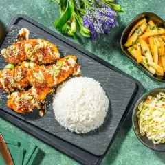Krispig koreansk kyckling med sesamfrön och salladslök, serverad med ris, pommes frites och kålsallad.