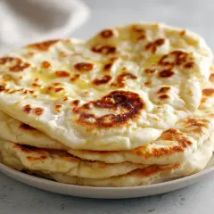 En stapel fluffigt, gyllene naanbröd, perfekt för ditt nästa naan recept. Smält smör glänser på toppen.