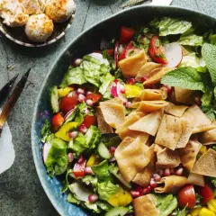 En fräsch fattoush-sallad med krispigt pitabröd, grönsaker och granatäppelkärnor. Bredvid ligger grillspett med kött.
