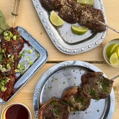 Grillad koreansk råbiff på spett, toppad med salladslök och chiliflakes. Serveras med limeklyftor och en skål sesamfrön.