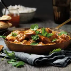 En skål med krämig kyckling tikka masala, toppad med koriander. Serveras med naanbröd och ris.