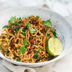 En skål med god wok med nudlar, grönsaker och en limeklyfta.