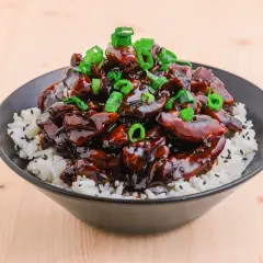 En skål med ris toppad med glansig teriyaki kyckling och strimlad salladslök.