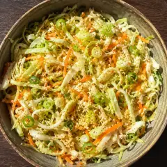 En skål med kålsallad vitkål, morötter och salladslök, toppad med sesamfrön.