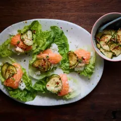 Läckra asiatiska tapas med lax, ris och gurka i salladsblad. En skål med marinerad gurka står bredvid.