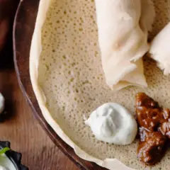 En hand tar en bit av en injera, en etiopisk rätt med kött och sås. Ett perfekt injera recept för en smakrik måltid.