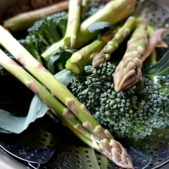 Grön sparris och broccoli ligger i en ångkorg, redo att ångkokas till perfektion.