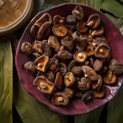 En skål med torkade shiitakesvampar, redo att ge en djup umami smak till din matlagning. Omgiven av gröna blad och en bambukorg.