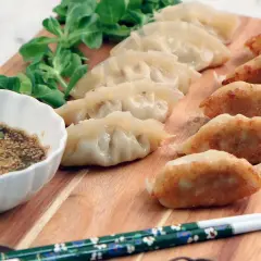 En rad gyllene, stekta dumplings och ångade dumplings serveras med en dippsås och grönsaker. Ett perfekt dumplings recept för en god måltid.