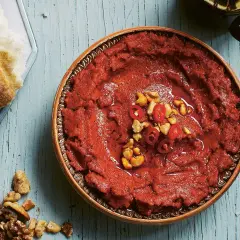 En skål med röd muhammara, toppad med chili och nötter, bredvid en bit bröd. Perfekt för ditt muhammara recept.