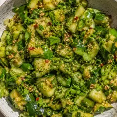 En skål med en matig sallad av gurka, örter och sesamfrön.