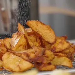 Krispiga potatisklyftor strös med salt efter frityr. Perfekt frityr temp för gyllene, läckra pommes.