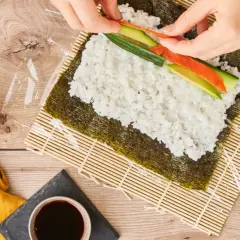 Händer lägger lax och gurka på ris för sushi maki.