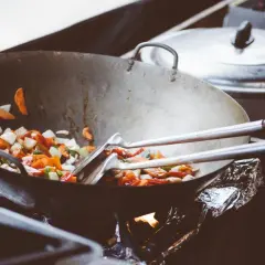 Wok med grönsaker som steks, med olika peppar sorter som ger smak. En gryta står i bakgrunden.