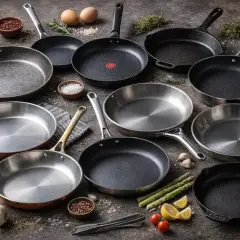 En samling stekpannor, redo för att steka med solrosolja. Ingredienser som sparris, vitlök och citron ligger utspridda.