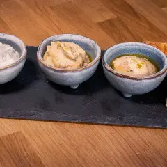 Tre skålar med dippar, som tzatziki och hummus, serveras med bröd. Perfekt för ett meze recept.