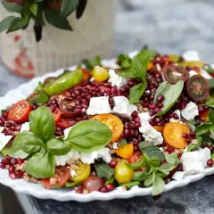 En färgglad sallad med granatäpple, tomater, fetaost och basilika, perfekt som sallad till grillat.