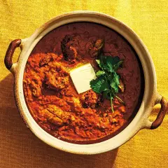En mustig kycklingrätt i en keramikskål, toppad med en smörbit och koriander. Detta är vad "masala" betyder – en kryddblandning som ger djup och smak.