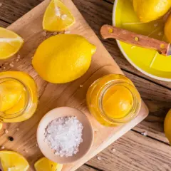 Gör ett läckert recept med inlagda citroner! Färska citroner, salt och pepparkorn förbereds på en träskärbräda.