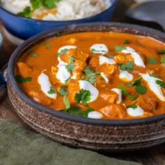 En krämig tikka masala med kycklingbitar, toppad med grädde och koriander. Serveras med ris och en skål yoghurt.