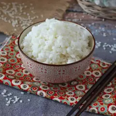 En skål med ångande ris, perfekt för egen sushi. Ätpinnar ligger redo på en färgglad duk.