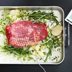 Råstek med örter och vitlök i ugnsform, redo för grillen. En digital termometer ger exakta grill tips för perfekt resultat.