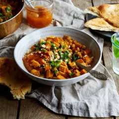 En skål med sötpotatiscurry med kikärtor, toppad med koriander och nötter. Serveras med naanbröd och en drink med mynta. Ett perfekt chilli recept.