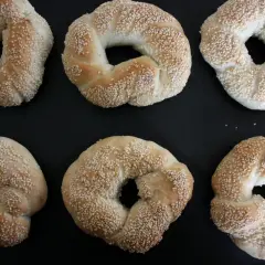 Sex gyllene simit, täckta med sesamfrön, ligger på en svart plåt. Perfekt för ett simit recept!