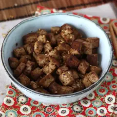 En skål med krispiga, tärnade tofu bitar, glaserade i en smakrik, glutenfri marinad och toppade med sesamfrön.