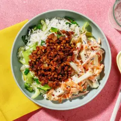 En skål med ris, pak choi sallad, och en kryddig topping. Bredvid ligger en gul servett och bestick.