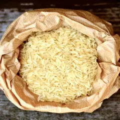 En påse med basmati eller jasminris ligger på en träyta. Riset är ljust och kornen är långa och smala.