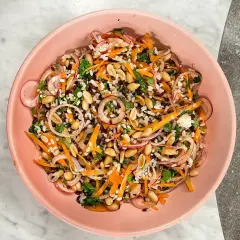 En färgstark ris sallad med jordnötter, morötter, rödlök och örter i en rosa skål.