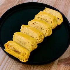 Skivor av gyllene japansk omelett, rullade och staplade på en svart tallrik.